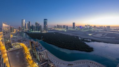 Skyscrapers on Al Reem and Al Maryah Island in Abu Dhabi day to night transition timelapse after sunset from above. Aerial panoramic cityscape from Al Reem Island with illuminated buildings clipart