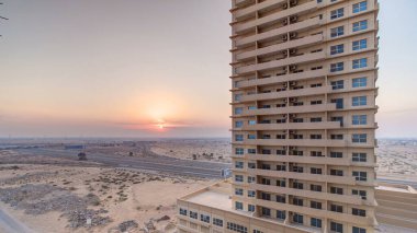 Ajman 'da gün batımı, çatıdaki zaman ayarlı hava manzarası. Birleşik Arap Emirlikleri 'ndeki bir iskan kulesinin arkasındaki turuncu bulutlu gökyüzünde akşam manzarası.