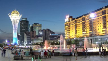 Bayterek Tower and fountain show day to night transition timelapse. People walking around after sunset. Skyscrapers on background. Monument and observation tower in Astana. Nur-Sultan city, Kazakhstan clipart