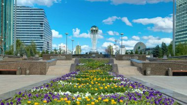 Nurzhol Bulvarı 'nda çiçekler. Arka planda Baiterek var. Kazakistan 'ın başkenti Nur-Sultan' da bir anıt, şehrin en önemli yerlerinden biri. Yazın mavi bulutlu gökyüzü