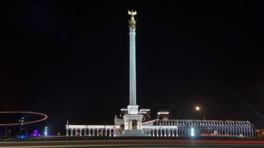 Stele anıtı Kazak Eli ve kuş Samruk geceleri ve Bağımsızlık Sarayı hiperhız ve trafik ön planda. Nur-Sultan şehri, Kazakistan