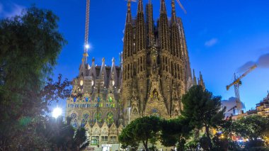 Sagrada Familia: İspanya 'nın Barcelona kentindeki Iconic Roma Katolik Kilisesi' nin Gündüzden Geceye Geçiş Süreci. Kuleler ve Turnalar Yakınlardaki Gölün Huzurlu Sularında Yansımaya Karşı Duruyor