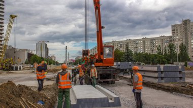 Yol inşaatında vinçle ezilmiş taşın üzerine beton plakalar yerleştiriliyor. Şapkalı ve üniformalı endüstriyel işçiler. Şehir caddesindeki tramvay raylarının yeniden inşası