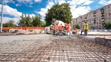 Tramvay rayları onarılan ve bakım süreleri yüksek olan yol inşaatı. Metal bir şebekeye beton dökülüyor. Kavşağın ortası. Arkaplanda yeşil ağaçlar