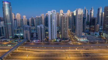 Dubai Marina gökdelenleri, güneş doğarken Dubai 'de JLT' den gündüz saatlerine kadar gökdelenler. Aydınlatılmış uzun gölgeli modern kuleler aşağı doğru ilerliyor ve Şeyh zayed yolunda trafik var..