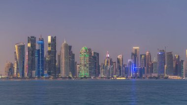 Doha şehir merkezi ufuk çizgisi günden geceye geçiş zamanı, Katar, Orta Doğu. Batı Körfezi 'ndeki aydınlık gökdelenler Körfez suyuna yansıyor.