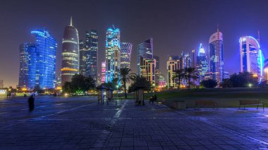 Doha 'nın yüksek katlı mahallesinde gece vakti hızlandırılmış hipervane, parktan görülmüş. Batı körfezinde aydınlatılmış gökdelenler ve palmiyeler