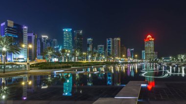 Geceleri Doha 'nın ufuk çizgisi. Yıldızlı gökyüzü Park Timelapse hiper hızından görünüyor, Katar. Aydınlatılmış gökdelenler ve kuleler çeşme suyuna yansıyor