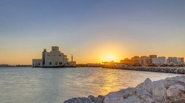 Güneş doğarken geçen balıkçı tekneleriyle Doha Limanı 'nda müze de arka planda. Doha, Katar, Orta Doğu. Önplanda taşlar.