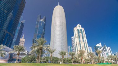 The skyline of Doha seen from Park timelapse hyperlapse, Qatar. Trees and palms on foreground. Modern skyscrapers and towers on background. Traffic on road clipart