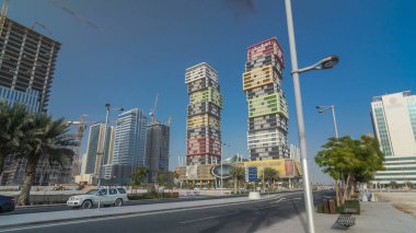Katar 'ın başkenti Lusail' de bulunan renkli Al Marina İkiz Kuleleri binasıyla Doha Skyline zaman çizgisi aşırı hızlanması. Palmiyeler ve ağaçlar. Yolda trafik vardı.