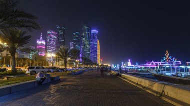 Geceleri Doha 'nın ufuk çizgisi Corniche Timelapse hiperlapse, Katar' dan görülebiliyor. Palmiyeler ve botlar yana. Aydınlatılmış gökdelenler ve kuleler