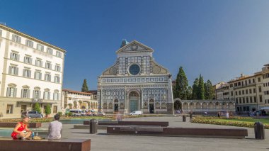 Santa Maria Novella Bazilikası 'nın Floransa' da eşkenar dörtgen zaman dilimi hiperhızlandırılmış görüntüsü. Çiçek yatakları ve yeşil çimenler. İnsanlar bankta oturuyor. Yazın mavi gökyüzü