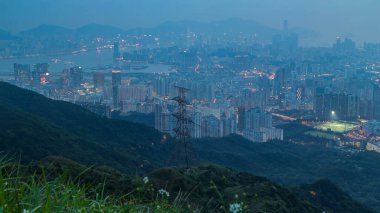 Day to night transition from Fei ngo shan Kowloon Peak night timelapse Hong Kong cityscape skyline. Tall buildings and power transmission lines. Green grass on the hill. clipart