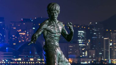 Bruce Lee monument hyperlapse in the night at the Avenue of stars, modern skyscrapers at the background in Hong Kong. Bruce Lee was the most influential and famous martial artist of the 20th century. clipart