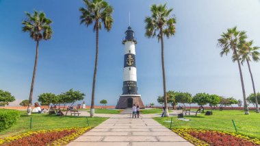 Miraflores Parkı 'ndaki deniz feneri manzaralı anıt zaman atlaması. Çiçekli ve palmiyeli yeşil çimenler. Güneşli bir günde sahil şeridi parkı. Lima, Peru
