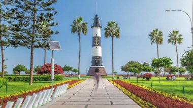 Miraflores Aşkı Parkı 'ndaki deniz feneri anıtı zaman atlaması. Çiçekli ve palmiyeli yeşil çimenler. Güneşli bir günde sahil şeridi parkı. Lima, Peru