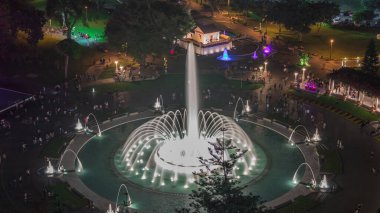 Park of the Reserve 'in en büyük çeşme kompleksi gece vakti aydınlanan renkli sihirli su devresi ile havadan görüntüsü. Yeşil çimenler ve ağaçlar.
