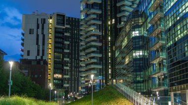 Milan Porta Nuova iş bölgesinden geceye geçiş zamanı. Gökdelenlerin pencerelerinde ışıklar. Yeşil çimen