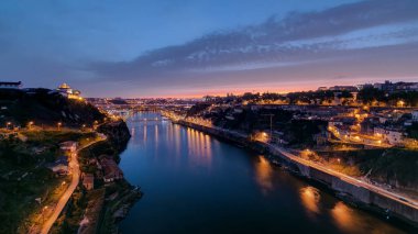 Day to night transition aerial view of the historic city of Porto, Portugal panoramic timelapse with the Dom Luiz bridge. Illuminated waterfront reflected in the river from above