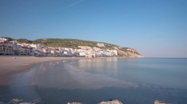 Sesimbra, Portekiz 'in küçük bir kasabasındaki iskeleden sahile, güneşli bir günde güneş batmadan önce mavi gökyüzü ile panorama zamanlaması hipervane