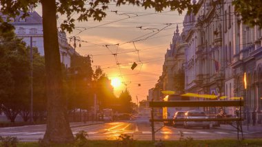Street with sunset in the Croatian capital Zagreb. People sitting on the bench near tree. Road traffic and tram rails