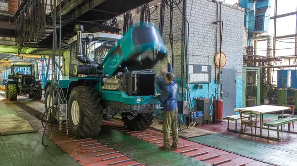 Konveyör montajı, traktörün gövdesini büyük endüstriyel fabrika zaman diliminde sahneleyecek. Traktörler montaj hattında ilerlerken tekerlekleri ve süspansiyonları kontrol et