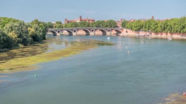 Toulouse, Fransa 'da Garonne River ve Pont Neuf saatleri. Rönesans kemer köprüsü mavi gökyüzünün altındaki suya Daurade Leydisi Bazilikası ile yansıyor. Yeşil ağaçlı rıhtım