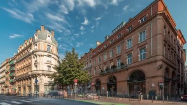 Toulouse, Occitanie, Fransa 'da Rue de Metz' in zaman çizelgesini gösteren panorama, tarihi cepheleri, dükkanları, kafeleri, trafiği ve mavi bulutlu gökyüzünü gösteriyor. Şehrin göbeğinde canlı bir şehir manzarası