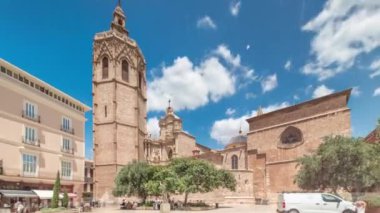 Valencia, İspanya 'da Plaza de la Reina' nın panoramik zaman atlaması. Tarihi bir kilise kulesi, hareketli kafeler ve sıcak Akdeniz mavi bulutlu gökyüzünün altında merkezi bir çeşme ile dolu canlı bir meydan..