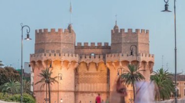 Serrans Kuleleri Torres de Serranos günden geceye Valencia, İspanya 'daki geçiş zamanı. Şehrin antik duvarlarından gelen büyük bir ortaçağ kapısı. İnsanlar tarihi bir dönüm noktasının yakınındaki bir köprüde yürüyorlar.