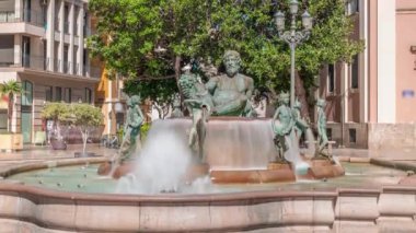 Valencia, İspanya 'daki ikonik Turia Pınarı ile birlikte Plaza de la Virgen' den Timelapse. Neptün heykeli Turia Nehri ve kanallarını temsil eder. İnsanlar yeşil ağaçlarla meydanda geziniyor.