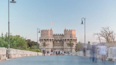 Serrans Kuleleri Torres de Serranos zamanapse Valencia, İspanya 'da. Şehrin antik duvarlarından gelen büyük bir ortaçağ kapısı. İnsanlar gün batımından önce tarihi bir dönüm noktasında akşam gökyüzünün altında bir köprüde yürüyorlar.