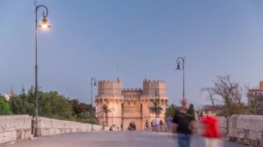 Serrans Kuleleri Torres de Serranos günden geceye Valencia, İspanya 'daki geçiş zamanı. Şehrin antik duvarlarından gelen büyük bir ortaçağ kapısı. İnsanlar tarihi bir yere yakın bir köprüde yürüyorlar.