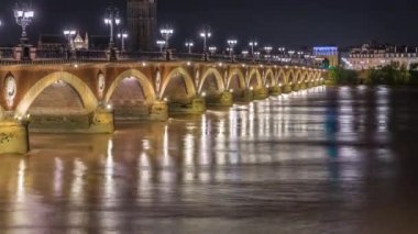 Fransa 'nın Bordeaux kentindeki Porte de Bourgogne' un aydınlatıldığı, gece Garonne Nehri üzerinde süslenmiş sokak lambaları olan Pont de Pierre Stone Köprüsü. Yansımaların ve şehir ışıklarının çarpıcı zamanlaması