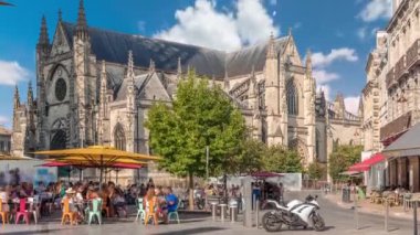 Bordeaux, Fransa 'daki Basilique Saint-Michel zaman çizelgesi, yüksek kulesi olan gotik bir simgedir. İnsanlar yakındaki kafeleri seviyor, yeşil ağaçların altında ve mavi bulutlu gökyüzü, şehrin canlı cazibesini yakalıyor.