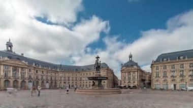 Place de la Bourse zaman atlaması Fransa 'nın Bordeaux şehrinde, Bulutlu mavi gökyüzünün altında klasik mimari ile çevrili Üç Zarafet Çeşmesi ile birlikte. Meydanda yürüyen insanlar.