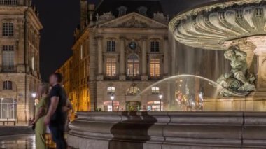 Place de la Bourse manzarası ve Fransa 'nın Bordeaux şehrindeki çeşme zamanı. Aydınlatılmış tarihi binalar büyük meydanın sınırında. Lokantada parlayan pencereler