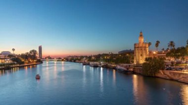İspanya, Seville 'deki Torre del Oro gözlem kulesi yakınlarındaki Guadalquivir Nehri boyunca yüzen bir tur teknesi. Günbegün geçiş zamanı, şehrin ışıkları su ve deniz manzarasını yansıtıyor.