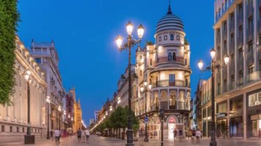 Avenida de la Constitucion, Seville, İspanya 'da günden geceye zaman dilimi. Iconic Adriatica binası gün batımından sonra parlıyor. Modern sokak lambaları, yayalar ve şehir atmosferine sahip tarihi mimari