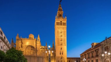 La Giralda ve Seville Katedrali günden geceye geçiş zamanı, gün batımından sonra altın ışıklarla parıldıyor. Tarihi çan kulesi, gotik detaylar ve Seville, İspanya 'da aydınlatılmış sokaklar.