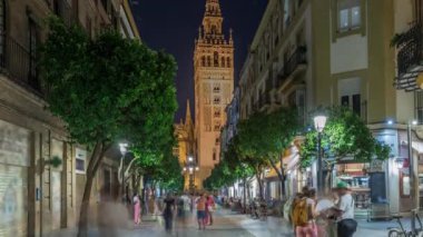 Barrio Santa Cruz 'un Seville, İspanya' daki gece zamanı. Arka planda Giralda kulesi aydınlanıyor. Turistler ve yerliler kafeler ve dükkanlarla dolu büyüleyici kaldırım taşları caddelerinde yürüyorlar..