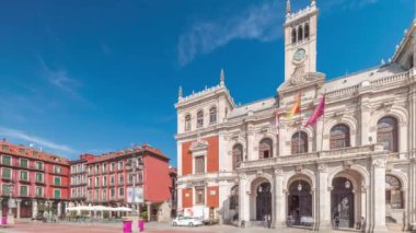 Panorama, Valladolid Plaza Belediye Başkanı Timelapse bayraklarıyla belediye binasının ön cephesini gösteriyor. Mavi gökyüzü ve şehrin göbeğindeki tarihi mimari. Yayalar bu merkez meydandan geçiyor..