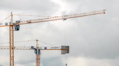 Bulutlu bir zaman dilimi olan bir bina kompleksi üzerinde çalışan ve hareket eden birkaç vinç de dahil olmak üzere büyük bir inşaat alanı. Büyük bulutlar geçip gidiyor.