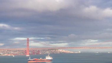 25 Nisan Köprüsü Ponte 25 de Abril, asma köprü. Tagus Nehri 'ni geçince Lizbon' u Almada 'ya bağlıyor. Önünde renkli dramatik bulutların altında bir kargo gemisi var.