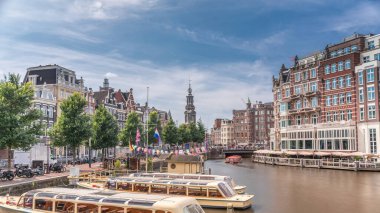 Amstel Nehri, rıhtım ve Munttoren kulesinin yer aldığı Amsterdam şehir merkezinin panoramik zaman atlaması. Tekneler bulutlu gökyüzünün altında ileri geri yüzerler. Köprüden manzaralı şehir manzarası. Hollanda