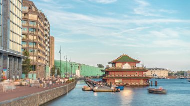 Sudaki pagoda şeklinde bir Çin restoranının hipervanesi, tarihi şehir merkezi binalarının ve günbatımında modern mimarinin arka planına karşı kurulur. Amsterdam, Hollanda