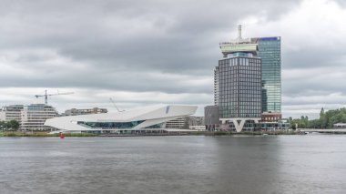 Amsterdam ufuk çizgisinin panoramik manzarasında, A 'dam Gözcü Kulesi ve Göz Filmleri Müzesi yer alıyor. Modern binalar dramatik yağmur bulutlarının altındaki suyu yansıtır. Amsterdam, Hollanda