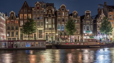 Gece vakti, Amstel Nehri 'nin kıyısındaki ünlü dans evlerinin panoramik zaman çizelgesi. Tekneli su kanalları. Hollanda, Amsterdam 'da ikonik simge ve seyahat noktası