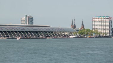 Amsterdam Merkez İstasyonu 'nun kıvrımlı çatısı ve Amstel Nehri zaman dilimi ile yakın görüntüsü. Bir feribot, bulutların hareketli olduğu güneşli bir gökyüzünün altında nehri geçer. Amsterdam, Hollanda